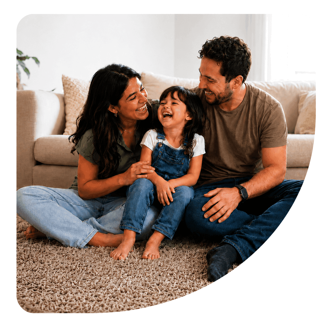 A mother, father, and young daughter laughing together on a rug at home