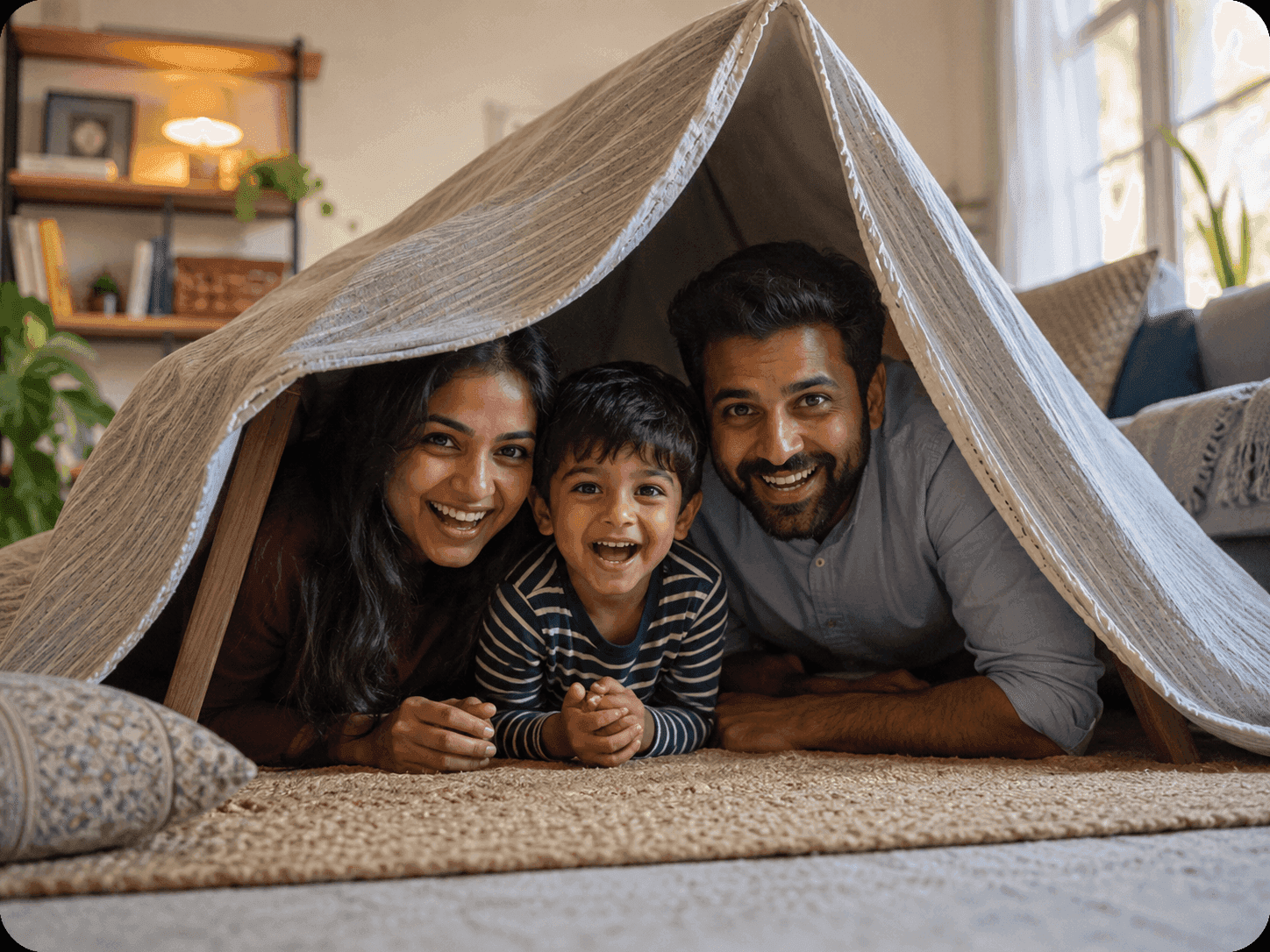 Two parents and their young son laughing together under a blanket fort at home