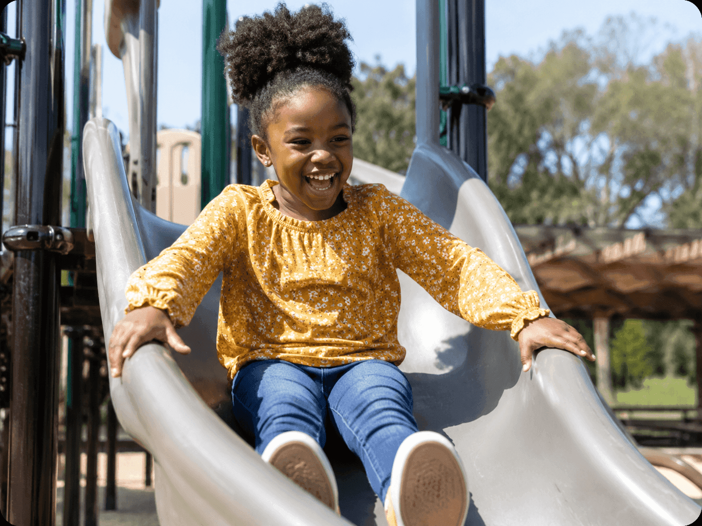 A child laughing as she comes down a playground slide